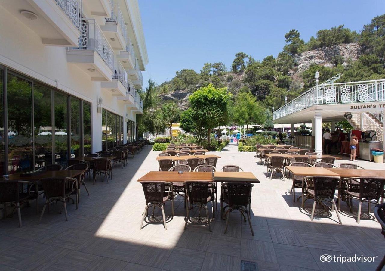 Miramor Hotel & Spa 안탈리아 외부 사진 The photo shows an outdoor dining area, likely at a restaurant or cafe. There are several tables with chairs arranged neatly on the paved ground, and some greenery, such as trees and plants, is visible in the background. The setting appears bright an